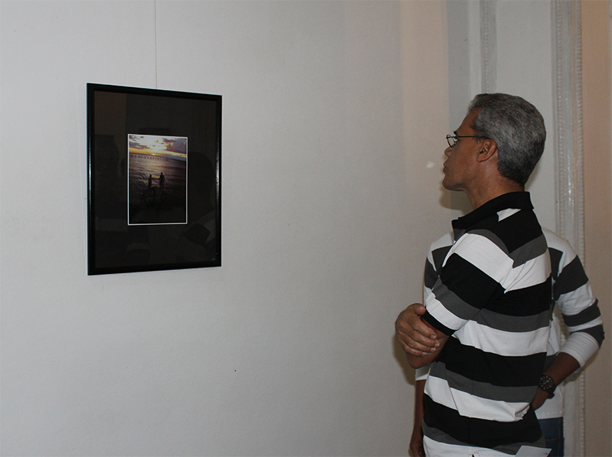 El reconocido artista de la plástica Wilfredo Milanés observa una de las fotografías que reflejan el atardecer manzanillero // Foto Marlene Herrera