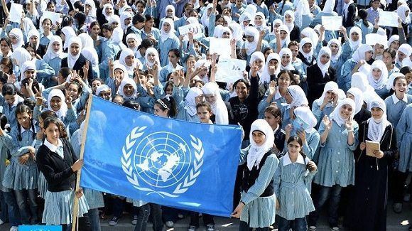 Niñas de Gaza posan al lado de la bandera de la UNRWA. Foto: Days of Palestine.