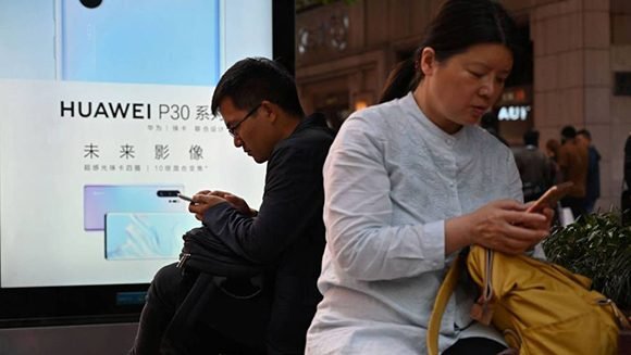 Usuarios con móviles junto a un anuncio de Huawei en Shanghái. Foto: AFP.