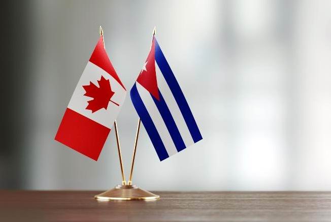 Cuban and Canadian flag pair on desk over defocused background. Horizontal composition with copy space and selective focus.