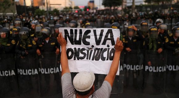 Un hombre sostiene una pancarta que dice «Nueva Constitución» mientras los policías montan guardia durante una protesta antigubernamental, en Lima, Perú , el 4 de febrero de 2023. // Foto: Reuters